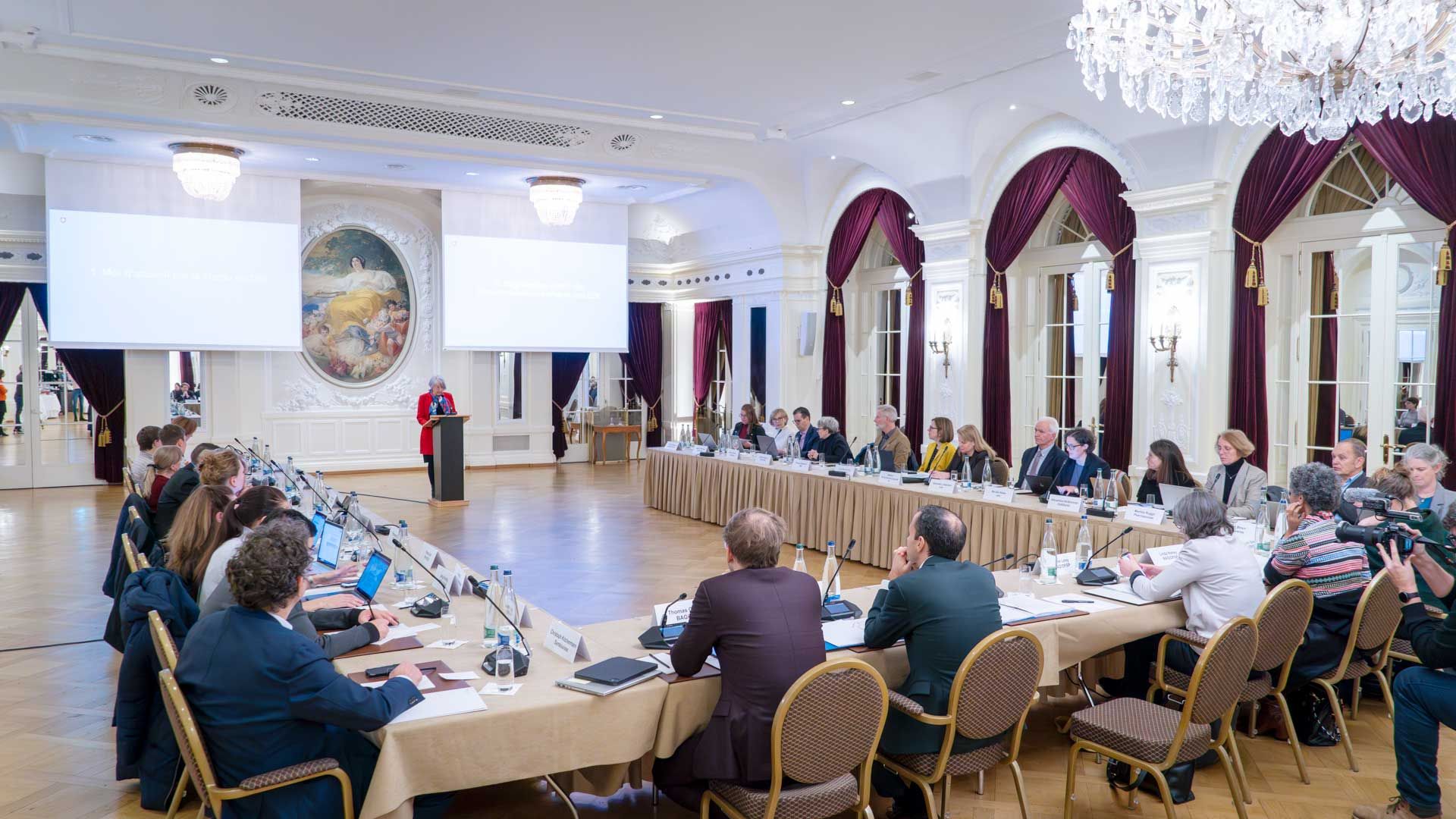 Bundesrätin Elisabeth Baume-Schneider steht an einem Rednerpult in einem grossen historischen Saal. Sie spricht zu rund dreissig Personen, die vor ihr an einem grossen Tisch sitzen und zuhören. 