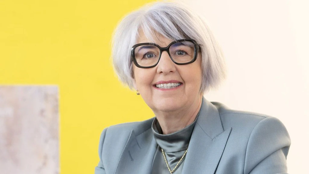 Portraitfoto von Bundesrätin Elisabeth Baume-Schneider. Sie trägt einen pinken Blazer und eine schwarze Hose. Ihren rechten Arm ist auf ein Regal gelegt. Sie lächelt in die Kamera. Der Hintergrund ist weiss.