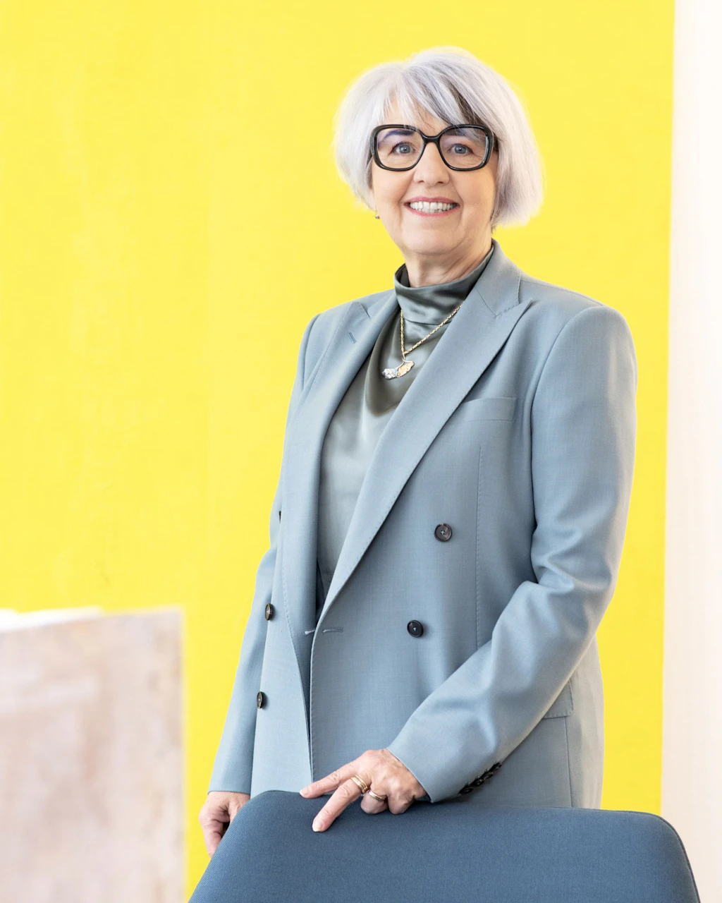 Portrait photograph of Federal Councillor Elisabeth Baume-Schneider. She is wearing a light grey blazer and smiling into the camera. A colourful painting hangs in the background.